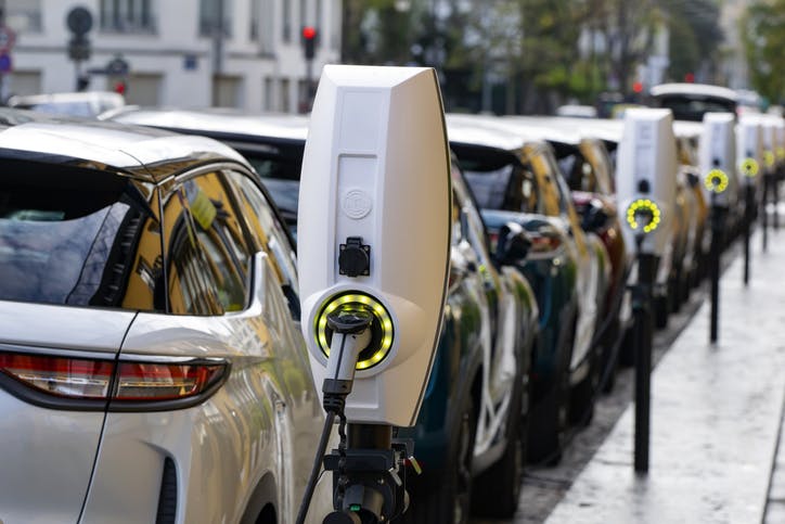 Image shows a row of cars parked curbside linked to electric charging points